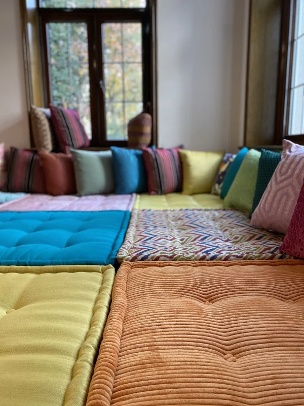 French Mah Jong daybed arranged with multicolored cushions, showcasing bold patterns and a cozy seating area.