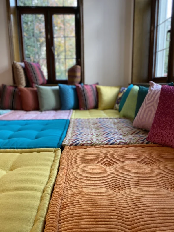 Vibrant Mah Jong daybed featuring colorful, tufted cushions in geometric and textured designs with a natural light backdrop.