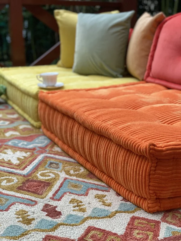 Orange Mah Jong sofa cushion with a vibrant patterned rug underneath, surrounded by outdoor greenery.