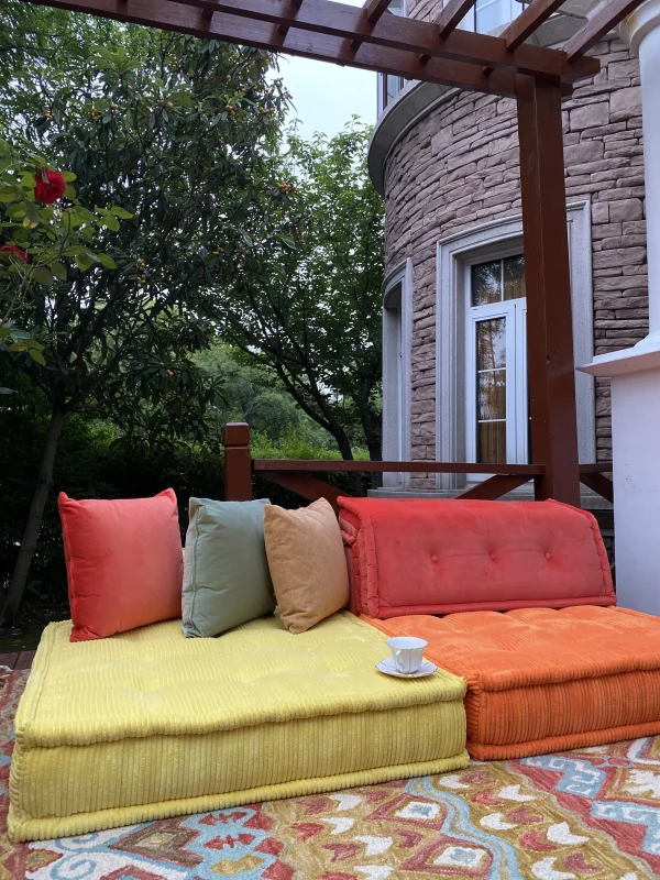 Mah Jong daybed in orange and yellow tones, styled with colorful cushions on a vibrant outdoor rug with floral decor.