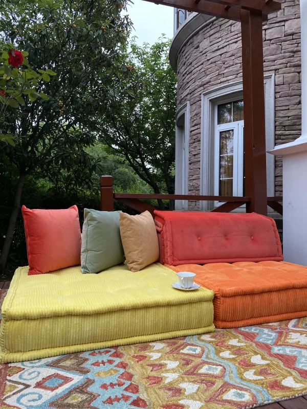 Orange and yellow Mah Jong sofa in an outdoor setting with greenery and a stone-clad house in the background.