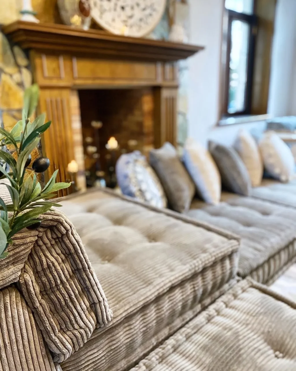 Close-up of a neutral beige Mah Jong Sofa in ribbed fabric, styled in front of a cozy fireplace with decorative elements.