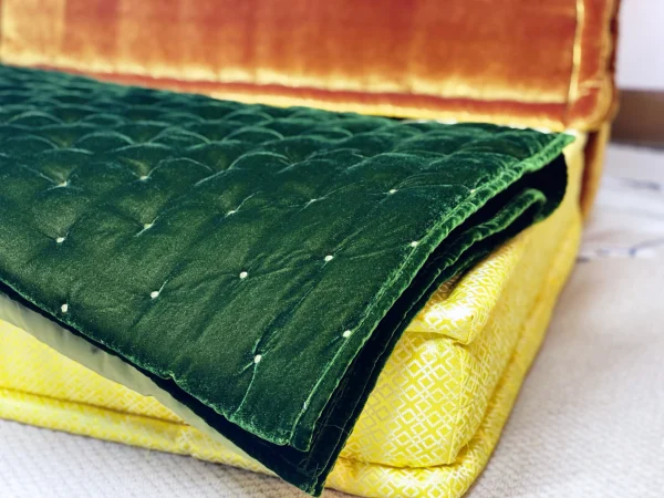 Close-up of layered cushions on Mah Jong sofa, featuring a green velvet quilt, yellow cushion, and orange backrest.