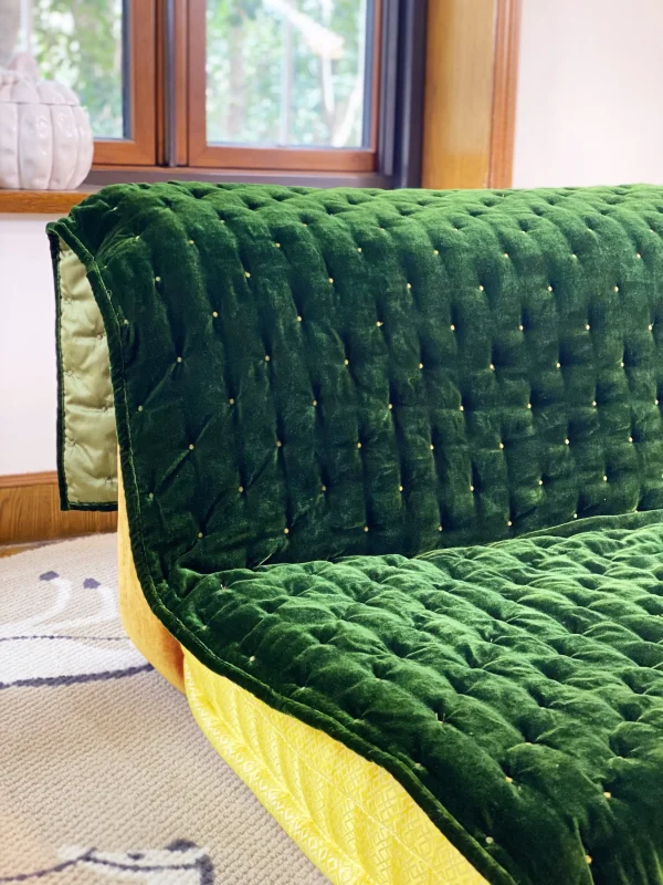 Mah Jong sofa featuring green velvet upholstery with yellow and orange cushion layers, placed near a bright window.