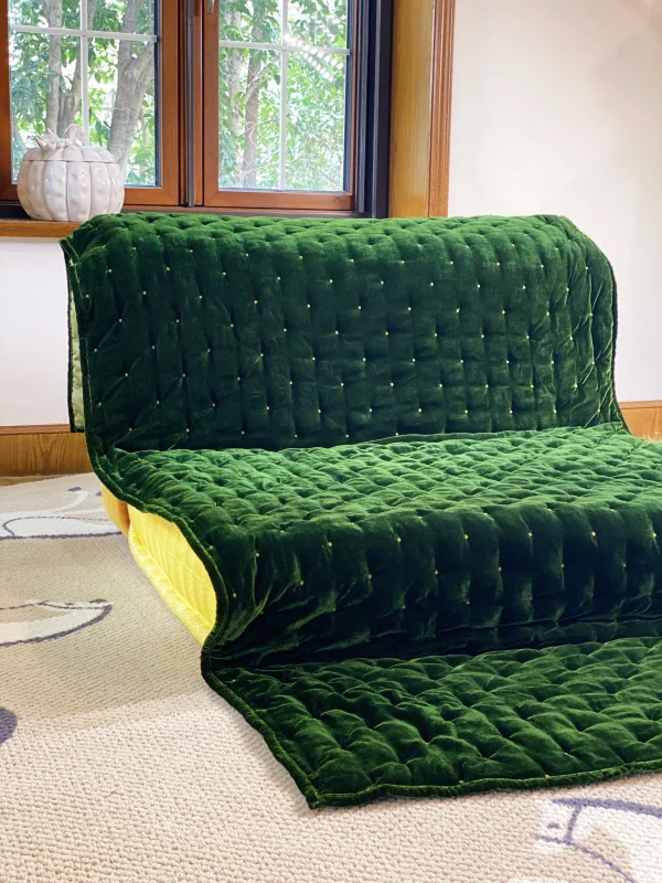 Full view of French daybed Mah Jong sofa with a green velvet quilted cover, placed in a bright living room.