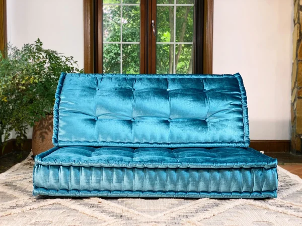 French Mah Jong sofa in vibrant teal velvet, styled against natural light and earthy tones for a warm ambiance.