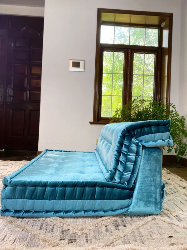 Teal velvet Mah Jong-style sofa displayed in a modern interior with bright windows and natural greenery.