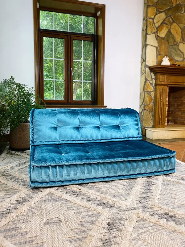 Side perspective of the teal velvet Mah Jong sofa, displayed in a bright and airy room with wooden windows and natural decor.