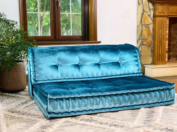 A luxurious teal Mah Jong-style sofa with plush cushioning, showcased in a rustic living room with bohemian decor.