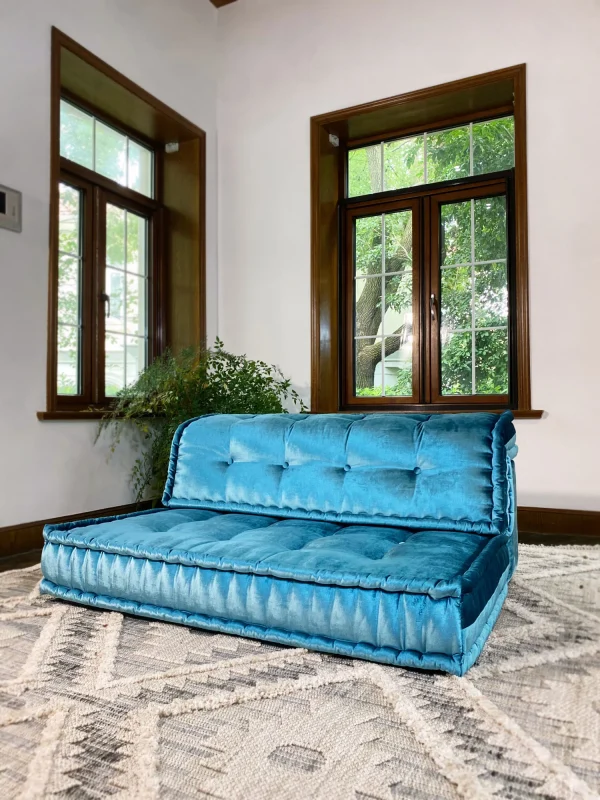 French Mah Jong daybed in teal velvet, styled near a fireplace and earthy indoor plants for a warm, inviting vibe.