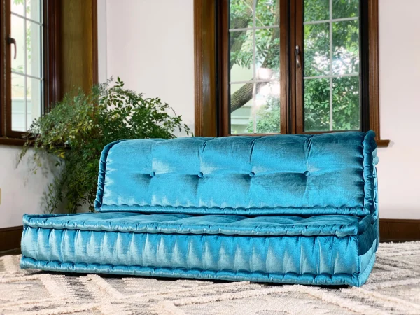 Angled side view of a teal velvet Mah Jong daybed sofa, highlighting its tufted details and soft fabric in a bright, modern space.