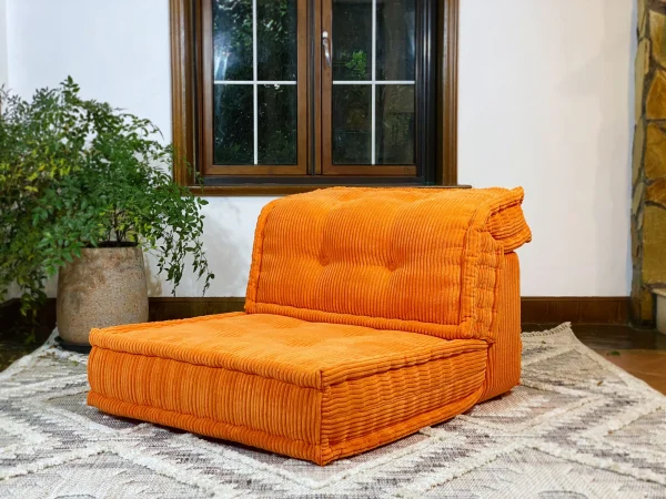 Mah Jong Daybed Sofa in bright orange placed in a serene living room with a potted plant accent.