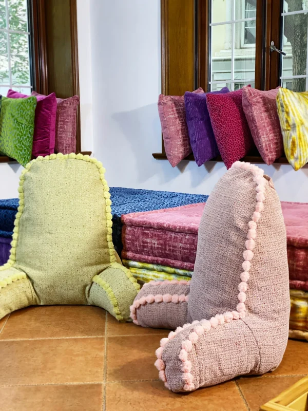 Close-up of pink and green backrest cushions with pom-pom accents on a colorful Mah Jong daybed.