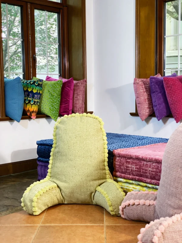 Mah Jong sofa styled with colorful cushions and a green pom-pom backrest cushion near a window.