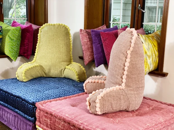 Colorful Mah Jong daybed setup with pink, blue, and yellow cushions near a window.