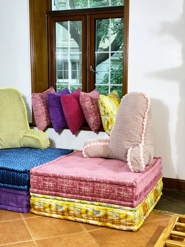 Side-by-side pink and green backrest cushions with pom-pom accents on a tiled floor.