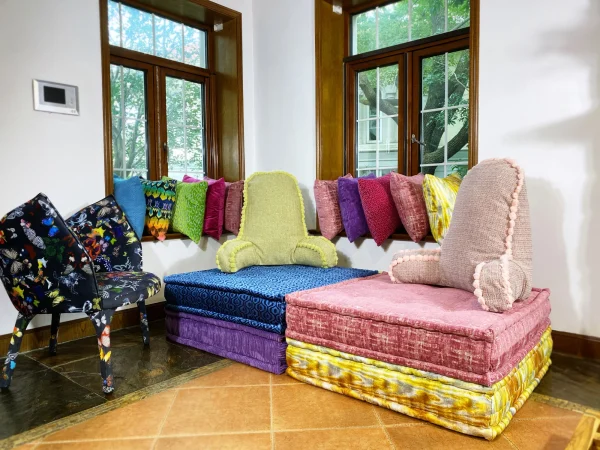 French Mah Jong daybed with colorful stacked cushions and a green pom-pom detailed backrest.