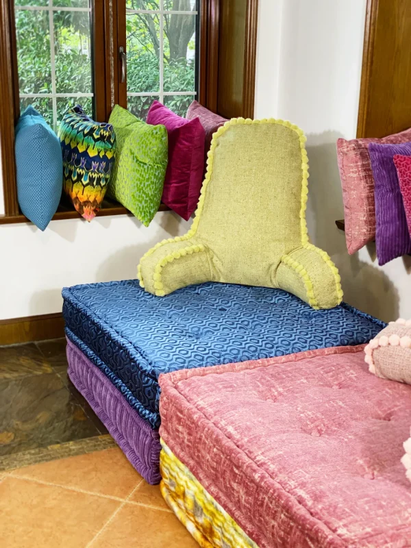 Two backrest cushions in pink and green with pom-pom accents, styled on a Mah Jong sofa.