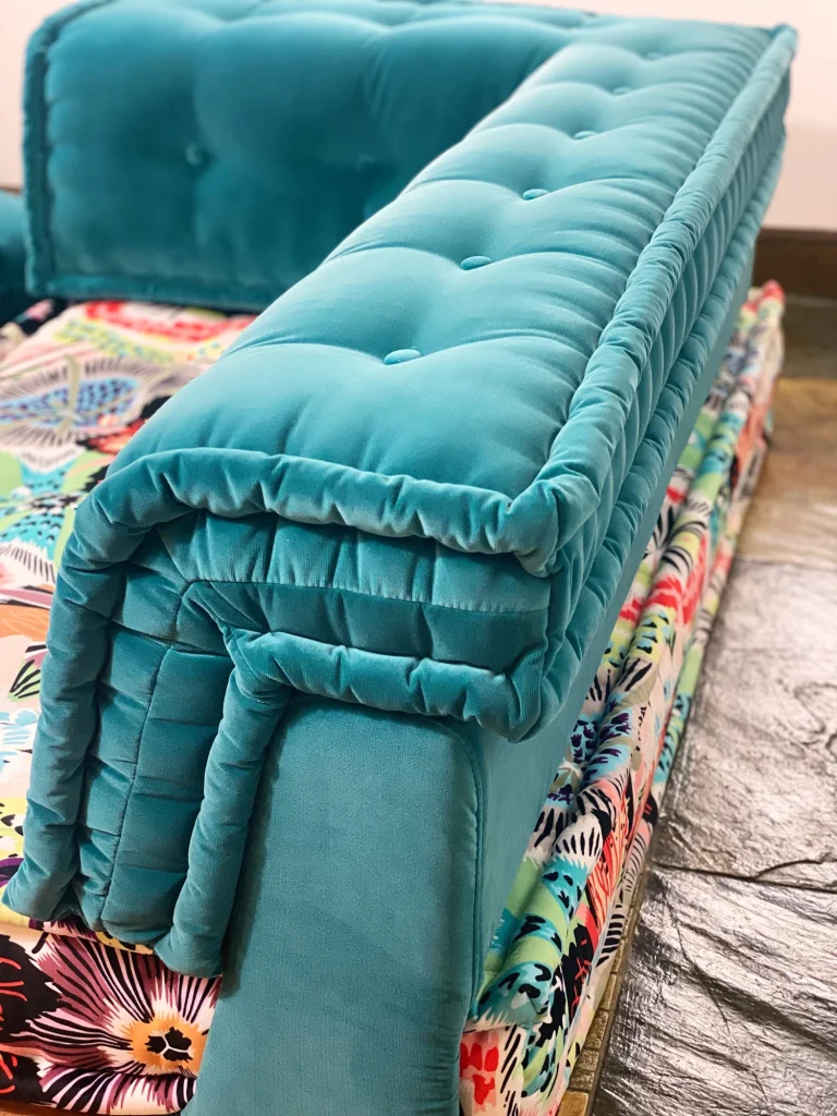 Luxury Mah Jong sofa armrest showcasing teal tufted velvet with vibrant floral cushion details.