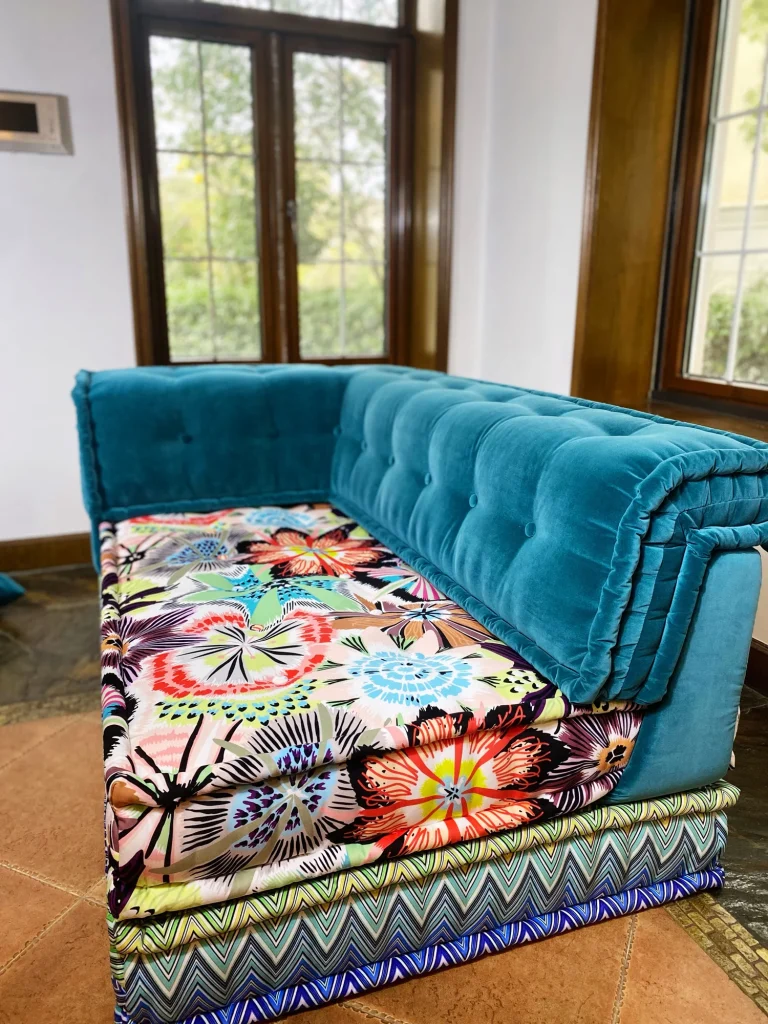 Side view of a Mah Jong French daybed sofa showcasing teal velvet upholstery and multicolored floral cushions.