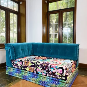 French daybed Mah Jong sofa with teal velvet tufted backrest and vibrant floral cushions.