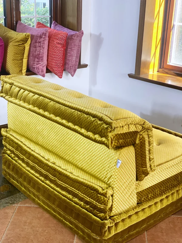 Rear view of the French Daybed Mah Jong Sofa in golden velvet with decorative pillows in the background.