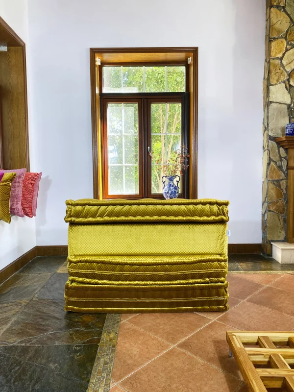 Rear view of the French Daybed Mah Jong Sofa in golden velvet fabric with a scenic window backdrop.