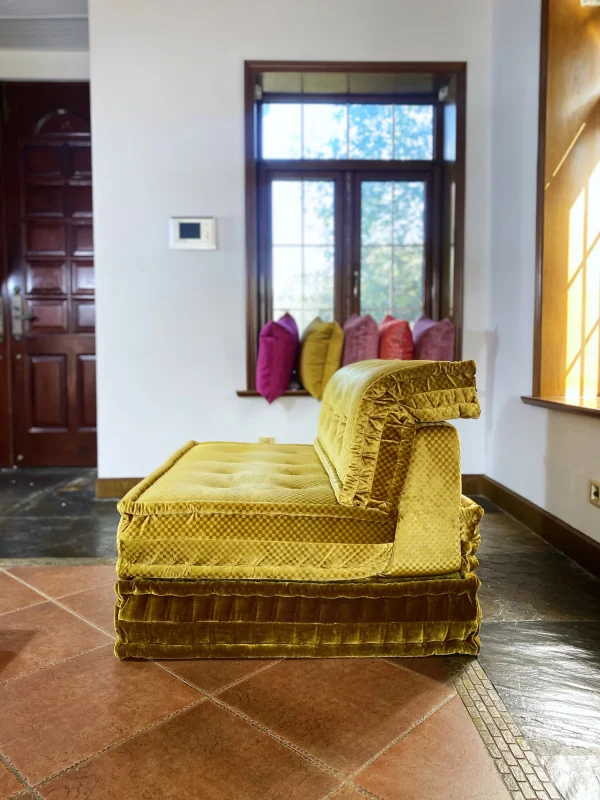 Luxurious French Mah Jong daybed in golden-yellow upholstery with a checkered texture, styled with colorful pillows in the background.