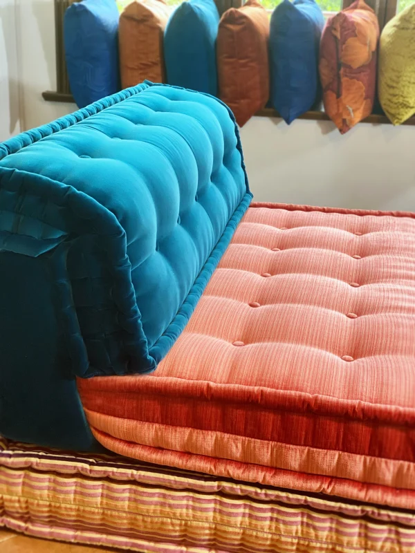 Mah Jong sofa with blue velvet backrest, pink cushions, and striped base in a bright interior.