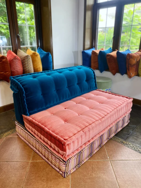 Mah Jong sofa with blue backrest, pink cushion, and striped base in a brightly lit room.