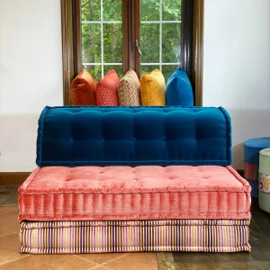 Mah Jong sofa with blue velvet backrest, pink cushions, and a striped base in a stylish room.