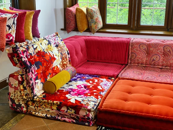 Red corduroy Mah Jong sofa module with a textured, tufted surface, surrounded by vibrant floral and paisley-patterned sections.