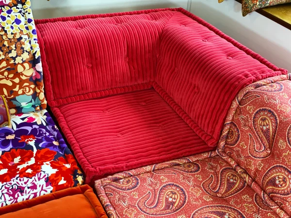 Close-up of a red paisley Mah Jong sofa module with intricate patterns and a tufted seat design, next to a large window.