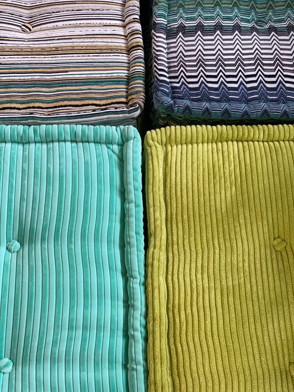 Close-up of teal and green Mah Jong sofa cushions with ribbed corduroy textures, styled on a vibrant patterned rug.