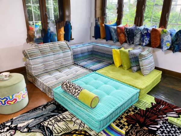 Bright Mah Jong sectional sofa in striped and teal patterns, styled with bold yellow and patterned cushions in a sunlit room.