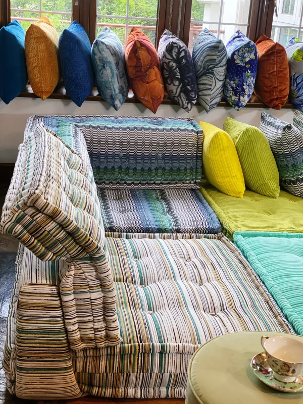 A sectional Mah Jong sofa in vibrant tones of stripes, greens, and blues, with large windows and colorful cushions in the background.