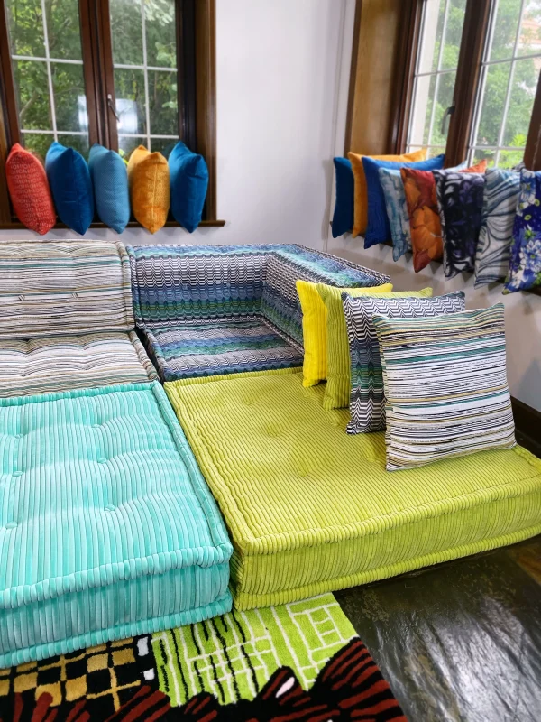 Elegant Mah Jong sofa with striped patterns and ribbed textures, styled near large windows with colorful cushions in a modern living room.