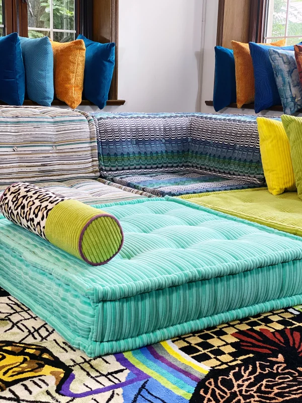 A cozy corner featuring a sectional Mah Jong sofa with striped and ribbed green upholstery, styled with bold yellow and multicolored cushions.