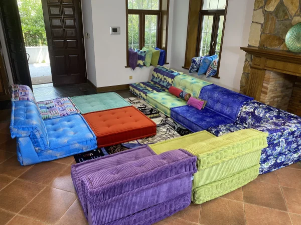 Multicolored modular Mah Jong sofa arranged in a spacious living room with large windows and a fireplace.