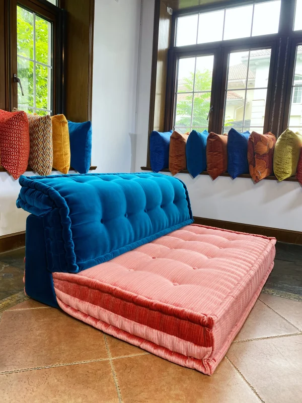 Side view of a Mah Jong-style sofa with coral pink and deep blue cushions in a modular design by a window.