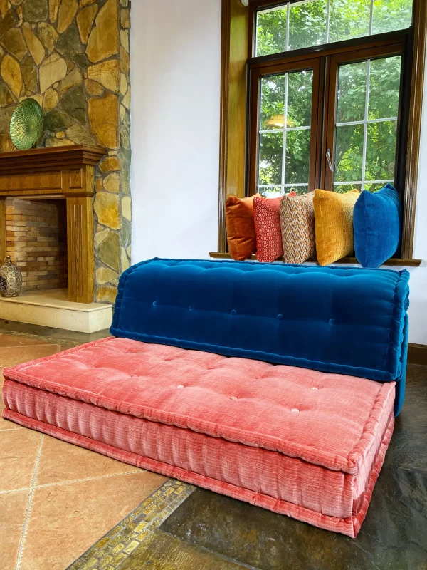 Mah Jong-style sofa with colorful cushions in a living room with a stone fireplace and natural lighting.