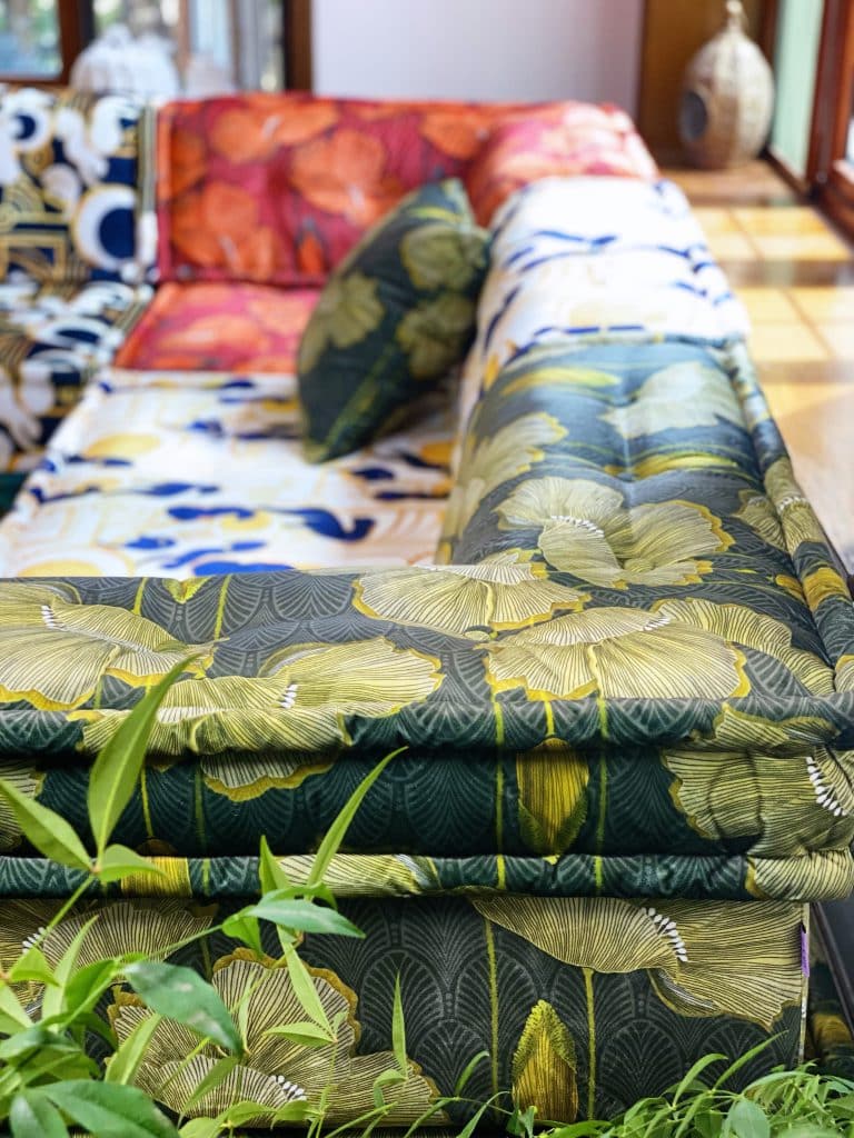 Close-up of a sofa module upholstered in a green and gold ginkgo leaf print, with a red floral module behind it