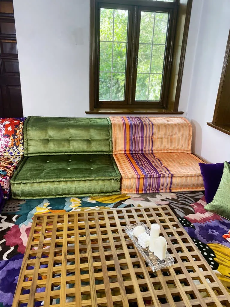 Modular sofa with an orange and purple striped module beside a green velvet module, above a floral rug and wood coffee table