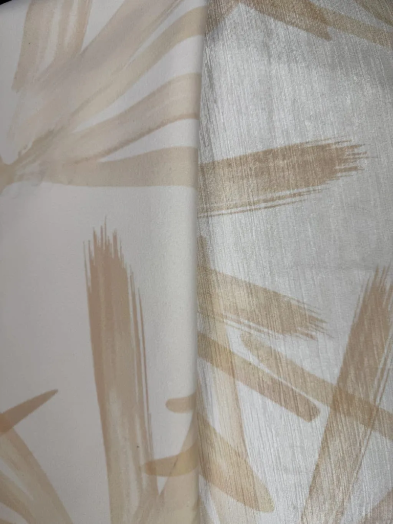 Close-up of folded palm print fabric samples in tan and cream, showing the brushstroke pattern