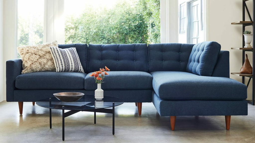 Apt2B custom sectional sofa in deep blue fabric with tufted cushions and tapered wood legs.