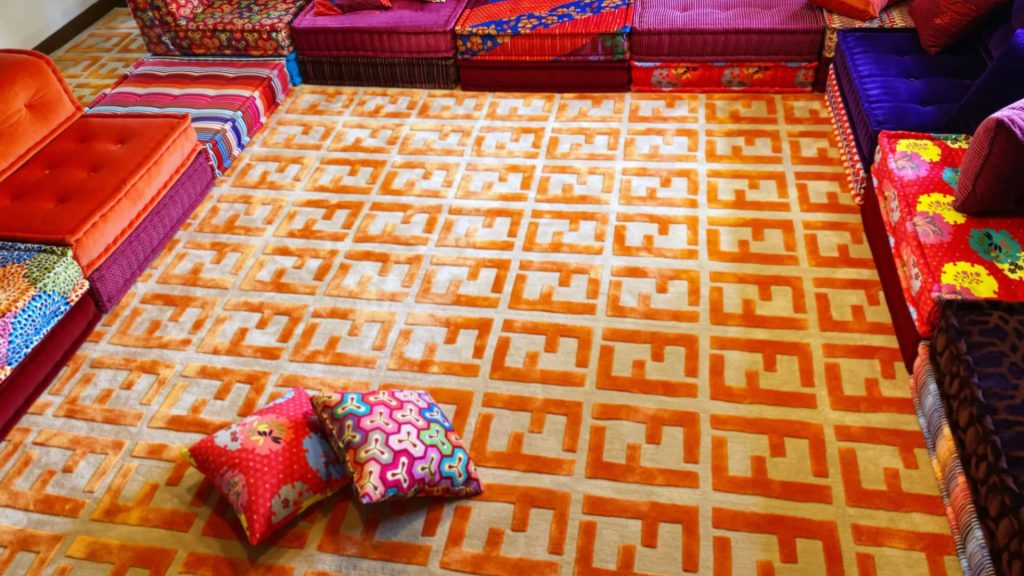 Overhead shot of an orange Fendi rug with colorful sofas.