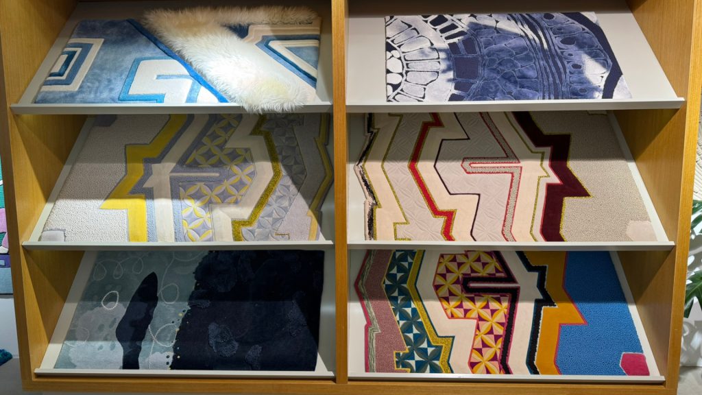 Six rug swatch materials on a shelf with different textures and colors.