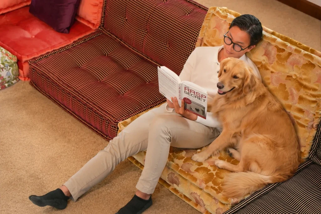 A man reads a book while his golden retriever sits beside him on an Adorn Croft Mah Jong sofa in floral velvet and plaid.