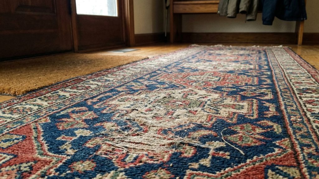 A closeup of a worn down rug in front of the main entrance of a house.