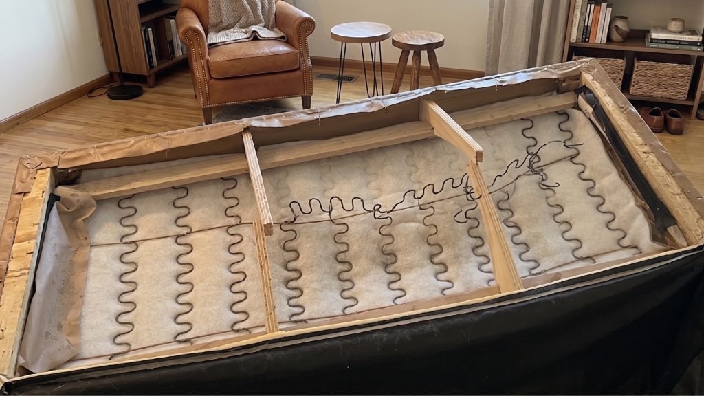 The underside of a broken sofa with a snapped wooden frame.